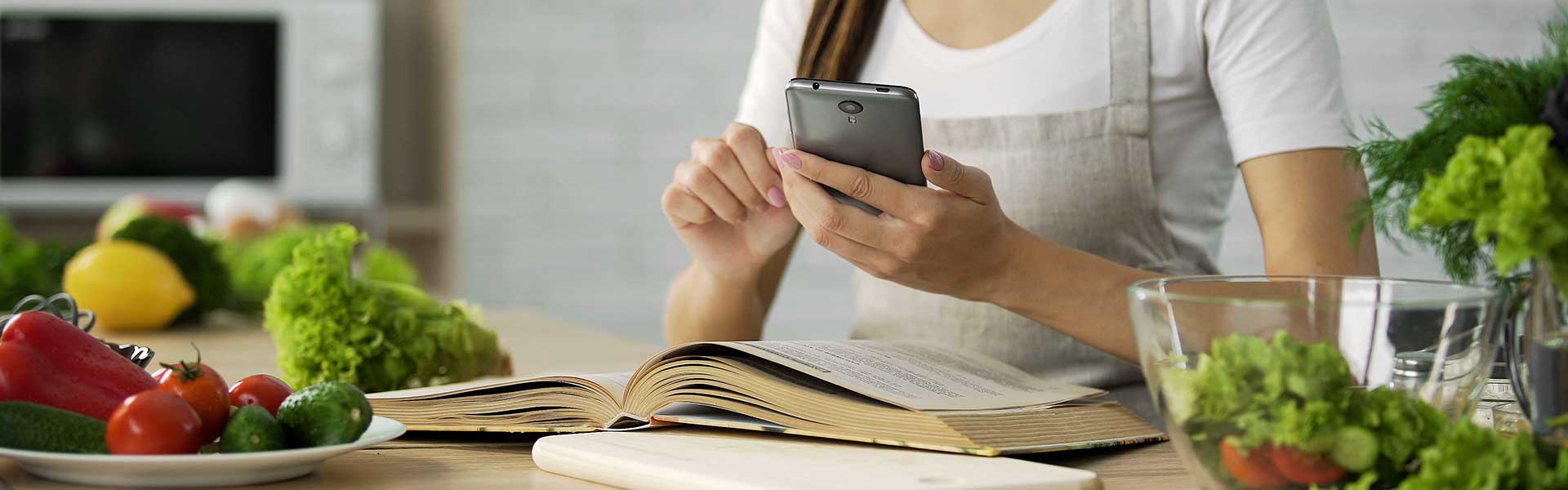 Woman looking at phone at a table with fruit and vegetables