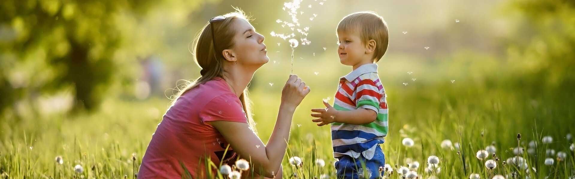 Mother blowing dandelions with young boy 