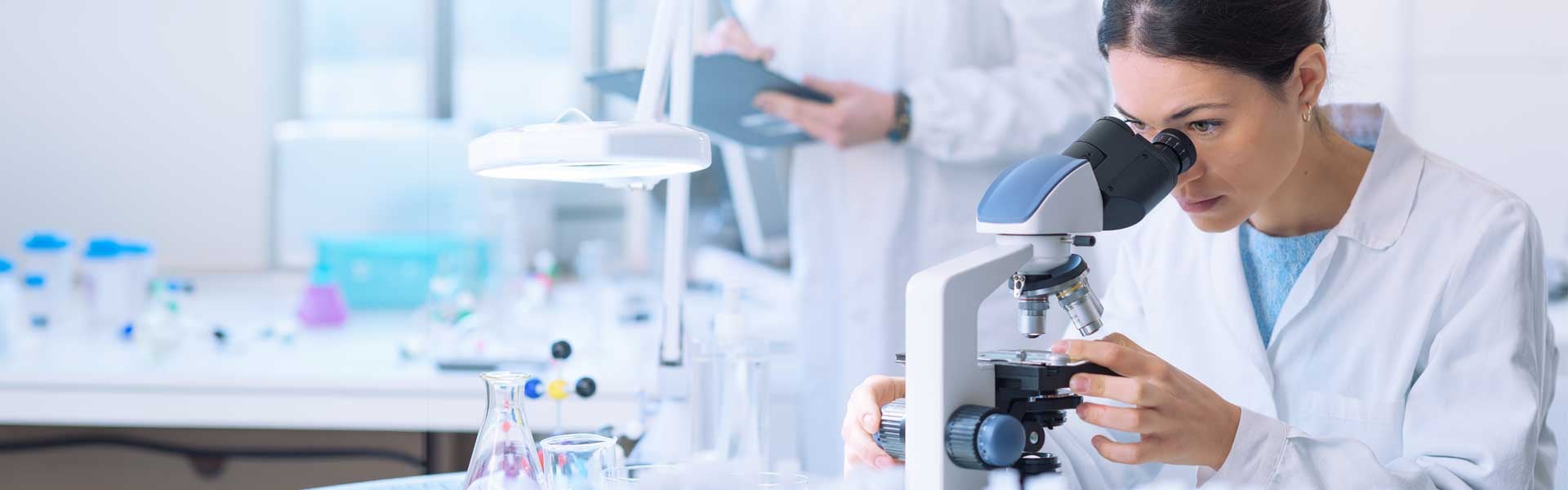 woman in lab looking down microscope