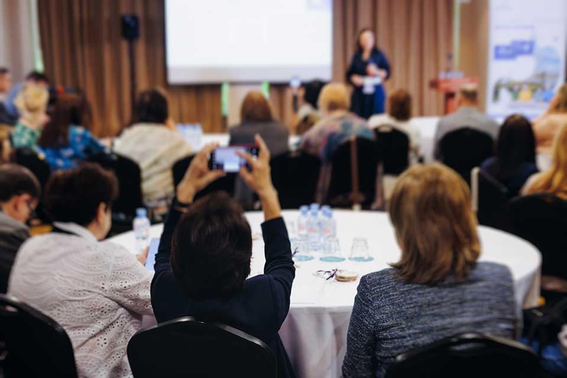Groups of people around round tables watching a presentation