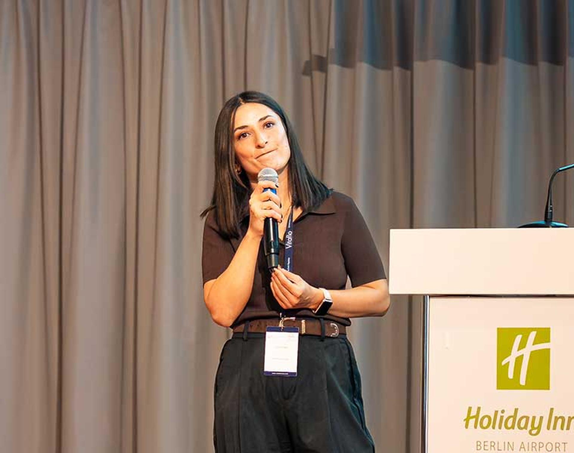 Dr. Fatma Ilgaz holding a microphone and speaking