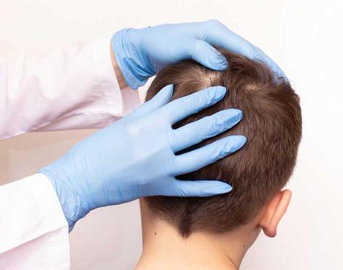 Person with gloves on examining the head of a young man