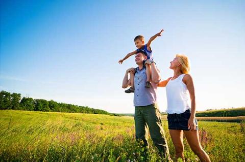 Family in a green field with a boy sitting on the shoulders of a man