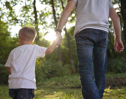Man and boy holding hands walking through woods